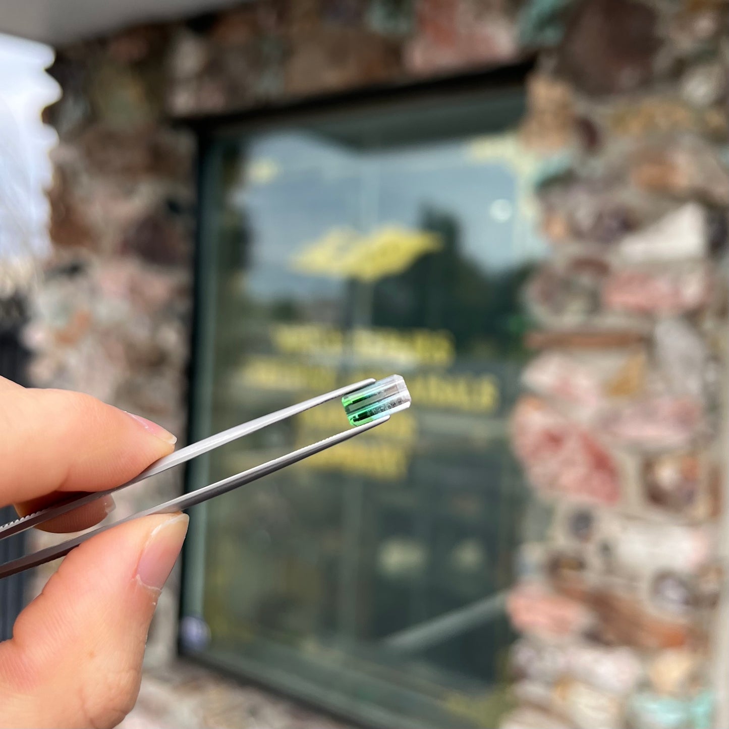 A loose, emerald cut tricolor tourmaline gemstone. The stone transitions from green to blue to white colors.