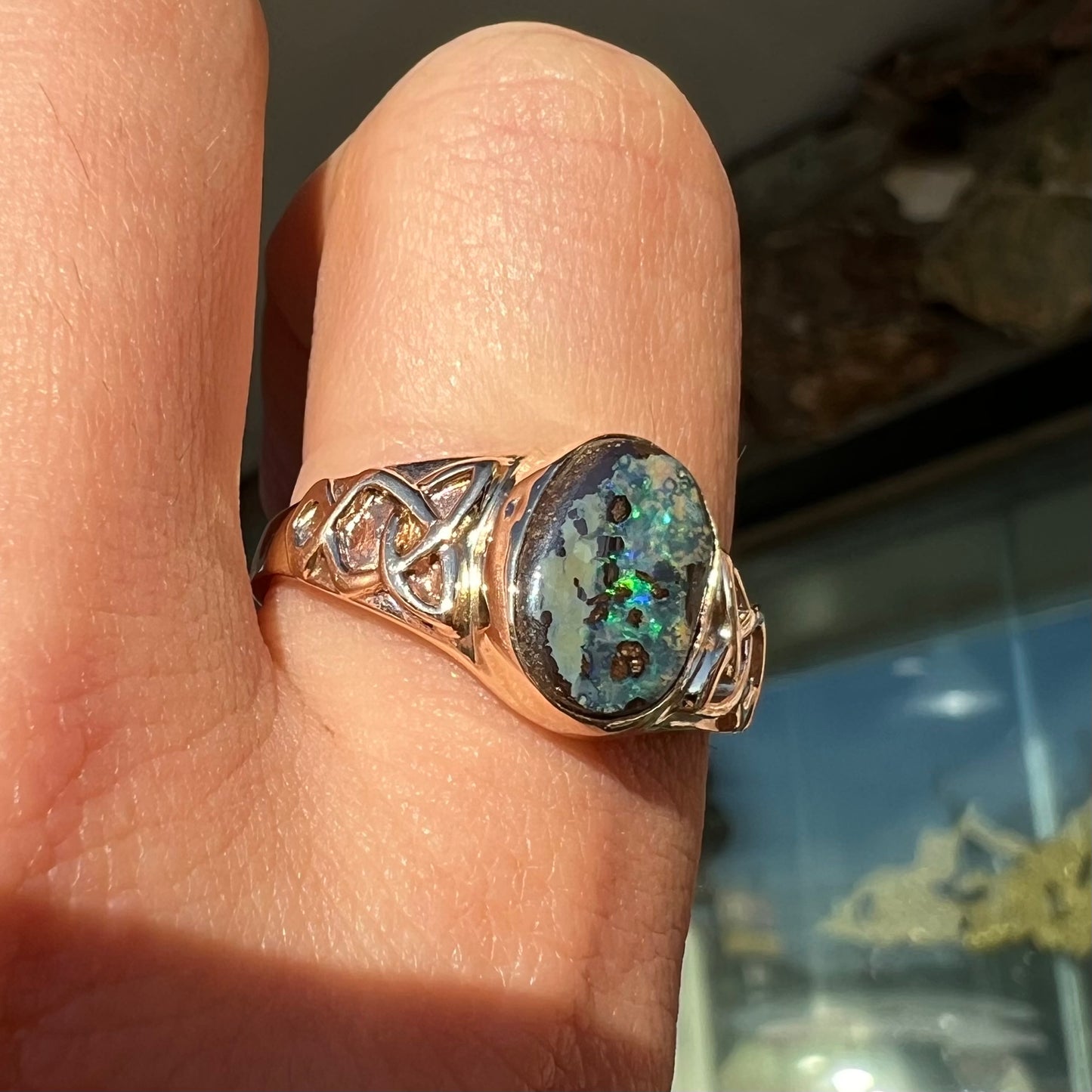 A unisex Celtic style natural boulder opal ring cast in yellow gold. The opal shines green and blue.