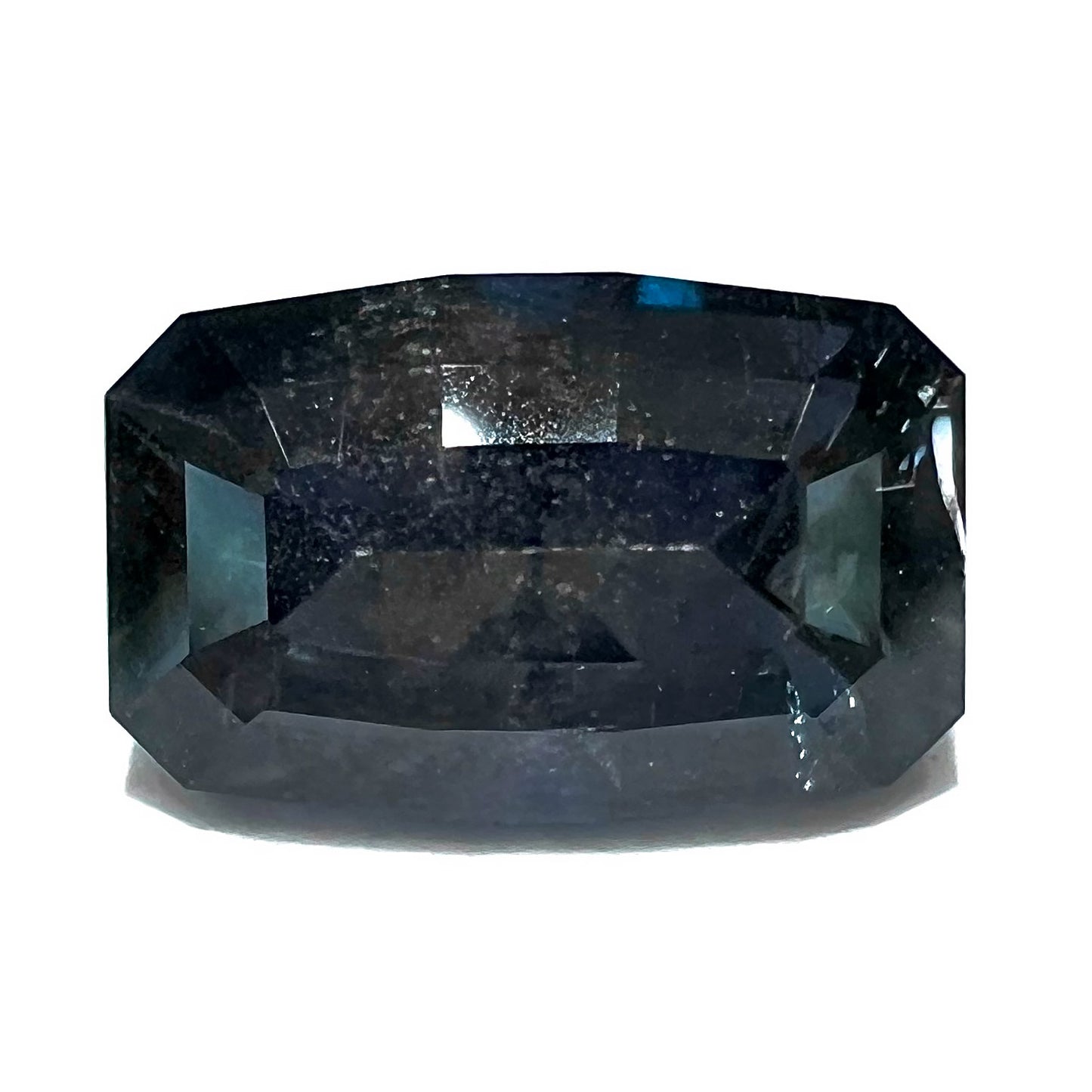 A loose, modified emerald cut, natural color change sapphire stone. The stone shifts from black to blue to purple to green.