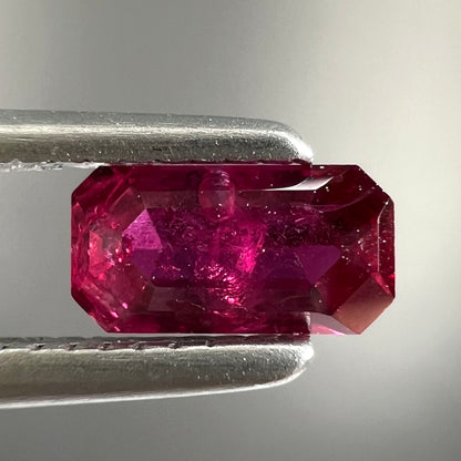A loose, purplish red natural ruby gemstone.  The stone is emerald cut.