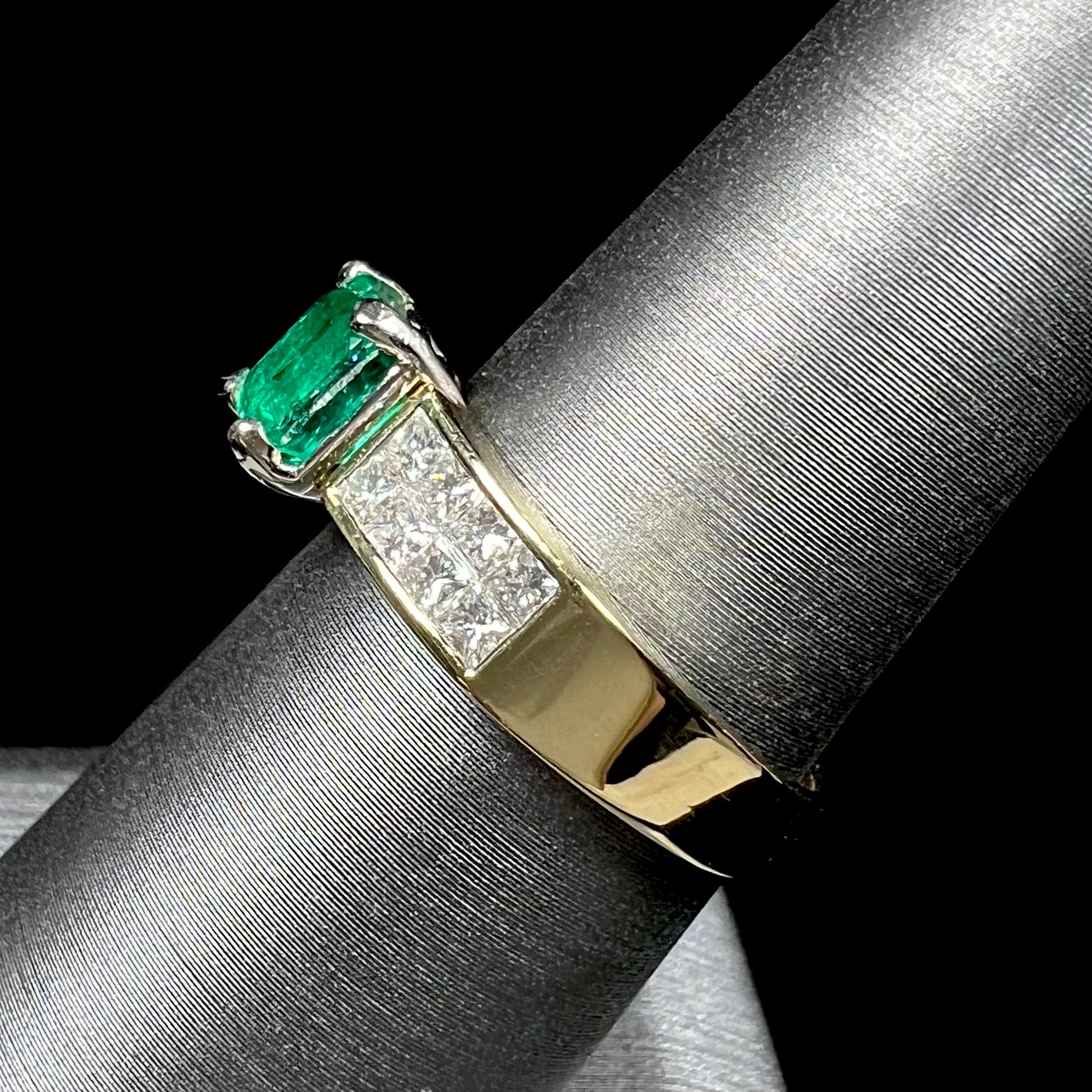 An 18 karat yellow gold ladies' emerald ring, channel set with princess cut diamonds.