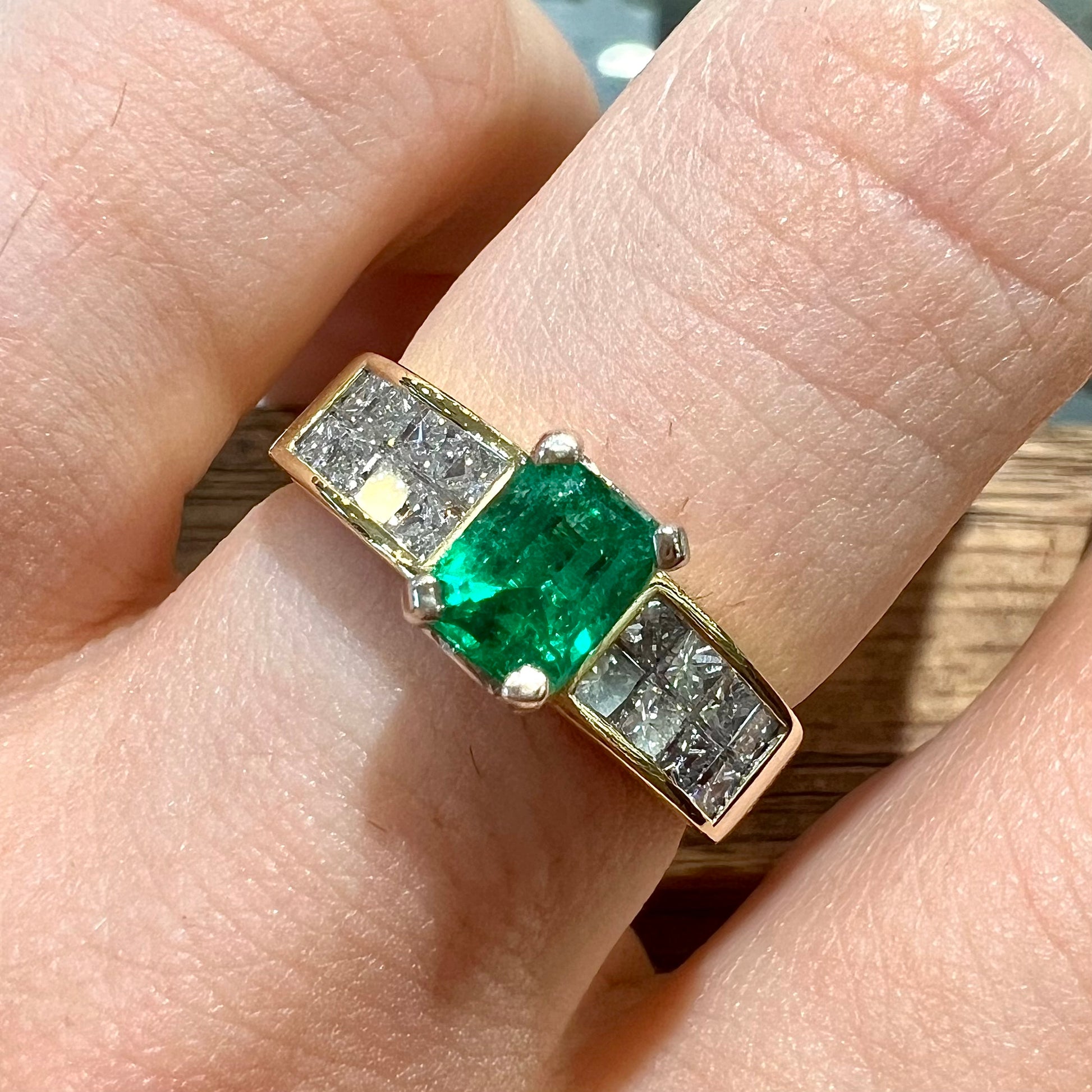 An 18 karat yellow gold ladies' emerald ring, channel set with princess cut diamonds.