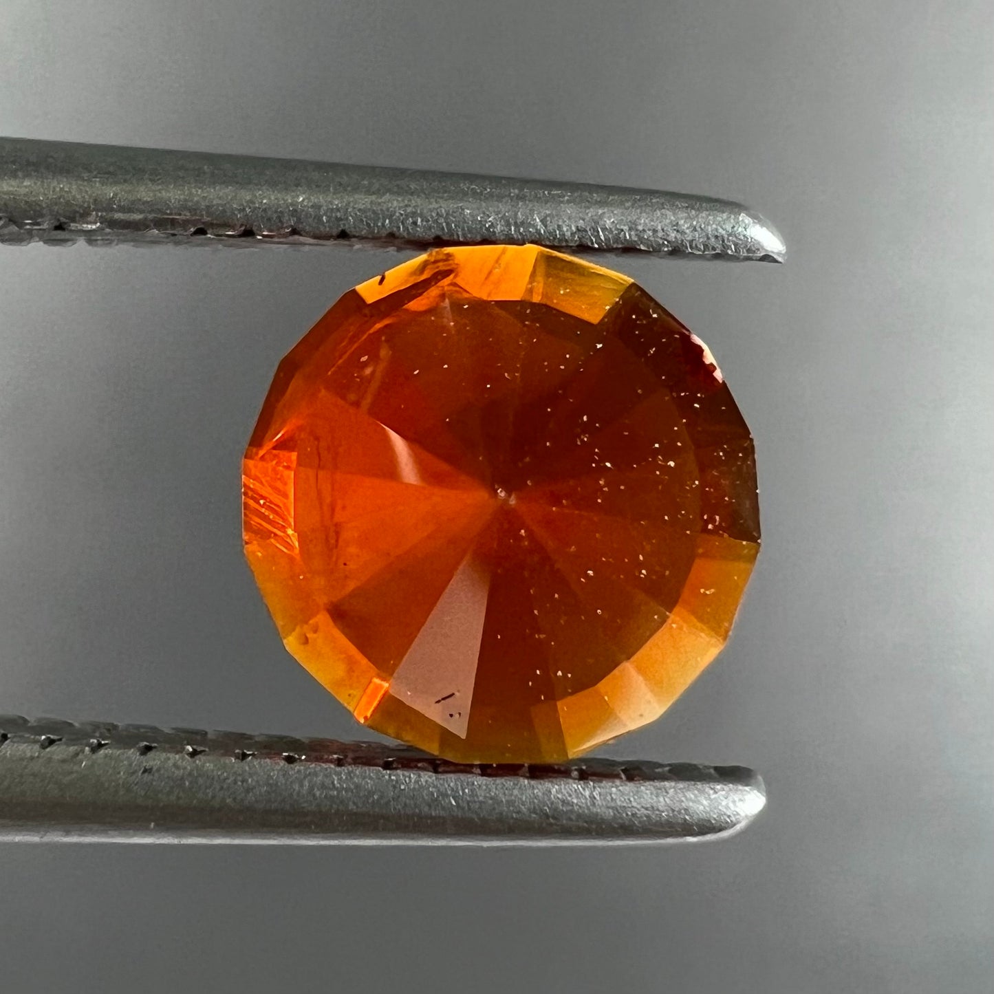 A faceted round cut natural Mexican fire opal stone. The stone is bright orange in color.