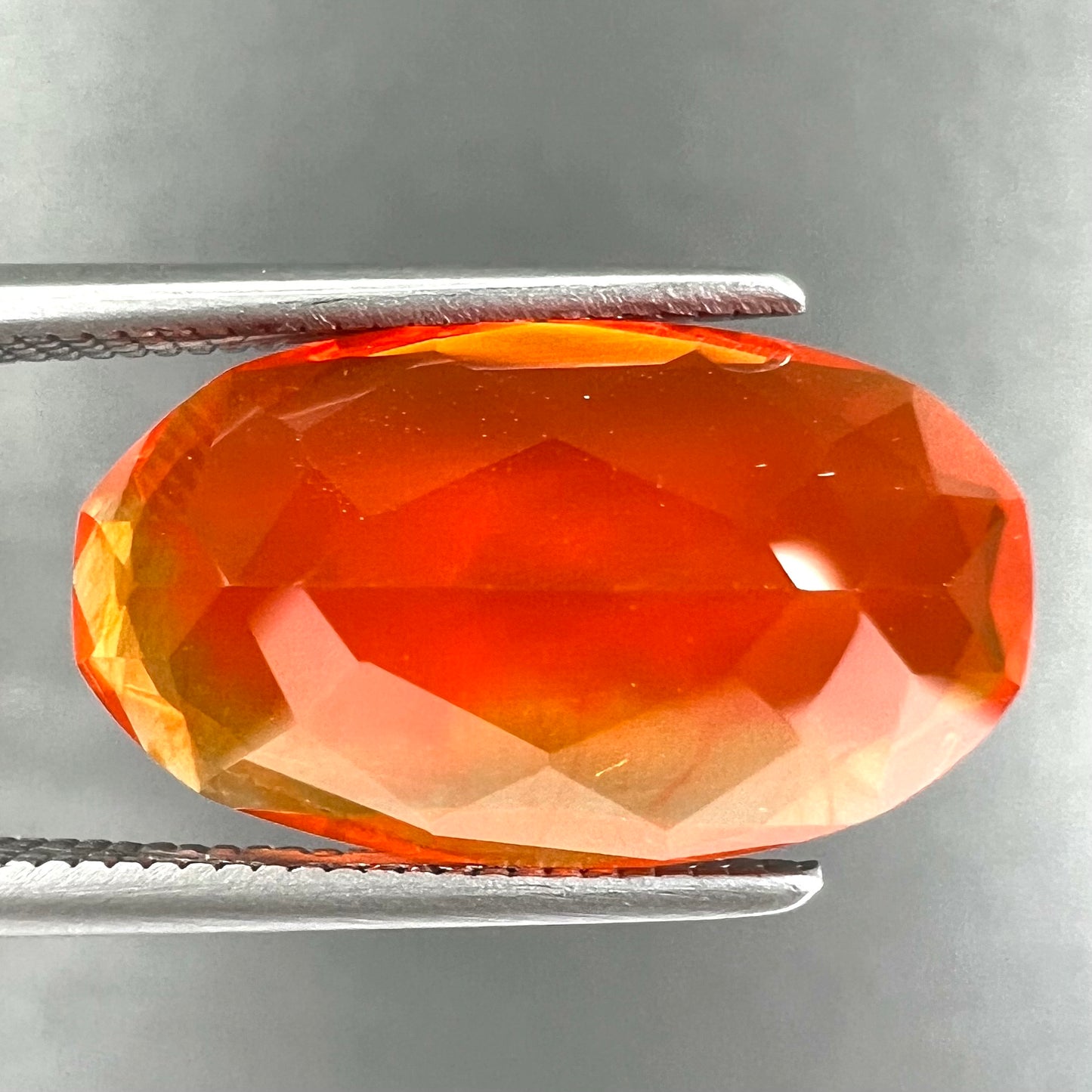 A loose, faceted oval cut Mexican fire opal stone. The stone is a bright orange color.