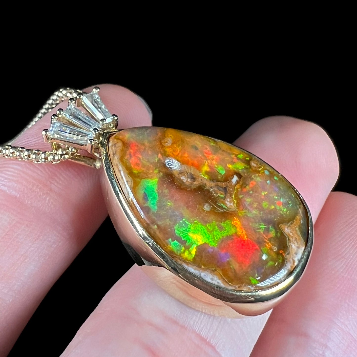 A unisex pear shaped fire opal pendant set with tapered baguette cut diamond accents in 18 karat gold.