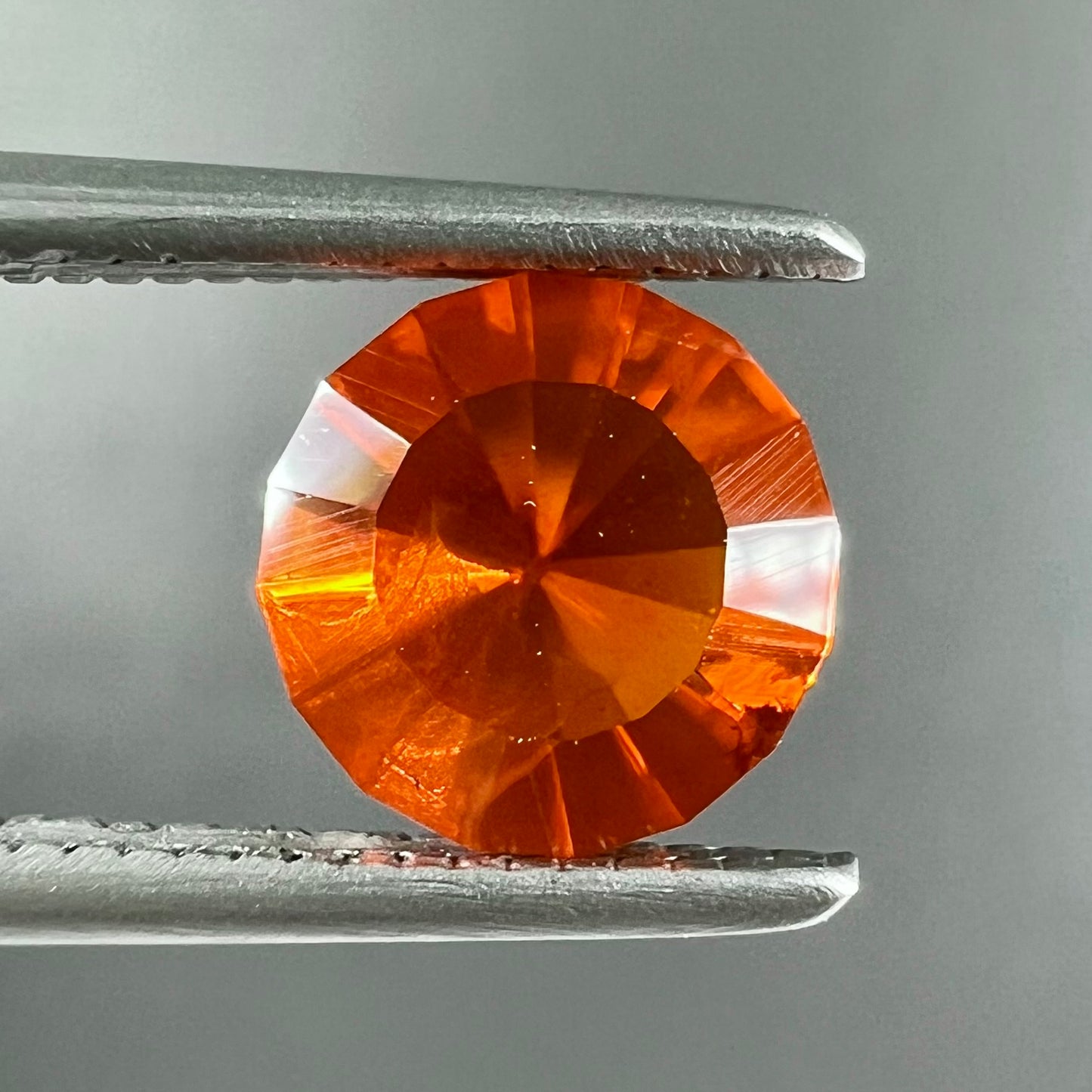 A faceted round cut natural Mexican fire opal stone. The stone is bright orange in color.