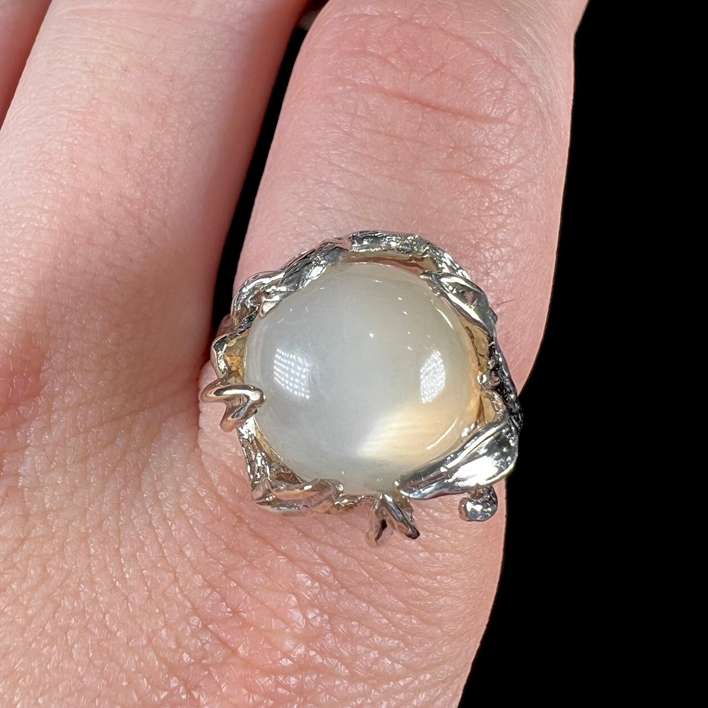 A ladies' organic style white gold moonstone ring. The moonstone shows white adularescence on a creamy white body color. Prongs resemble leaves holding the stone.