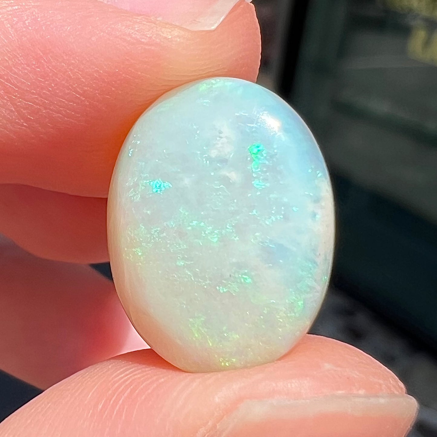 An oval cabochon cut white opal stone from Coober Pedy, Australia. The opal has subtle colors of green and blue.