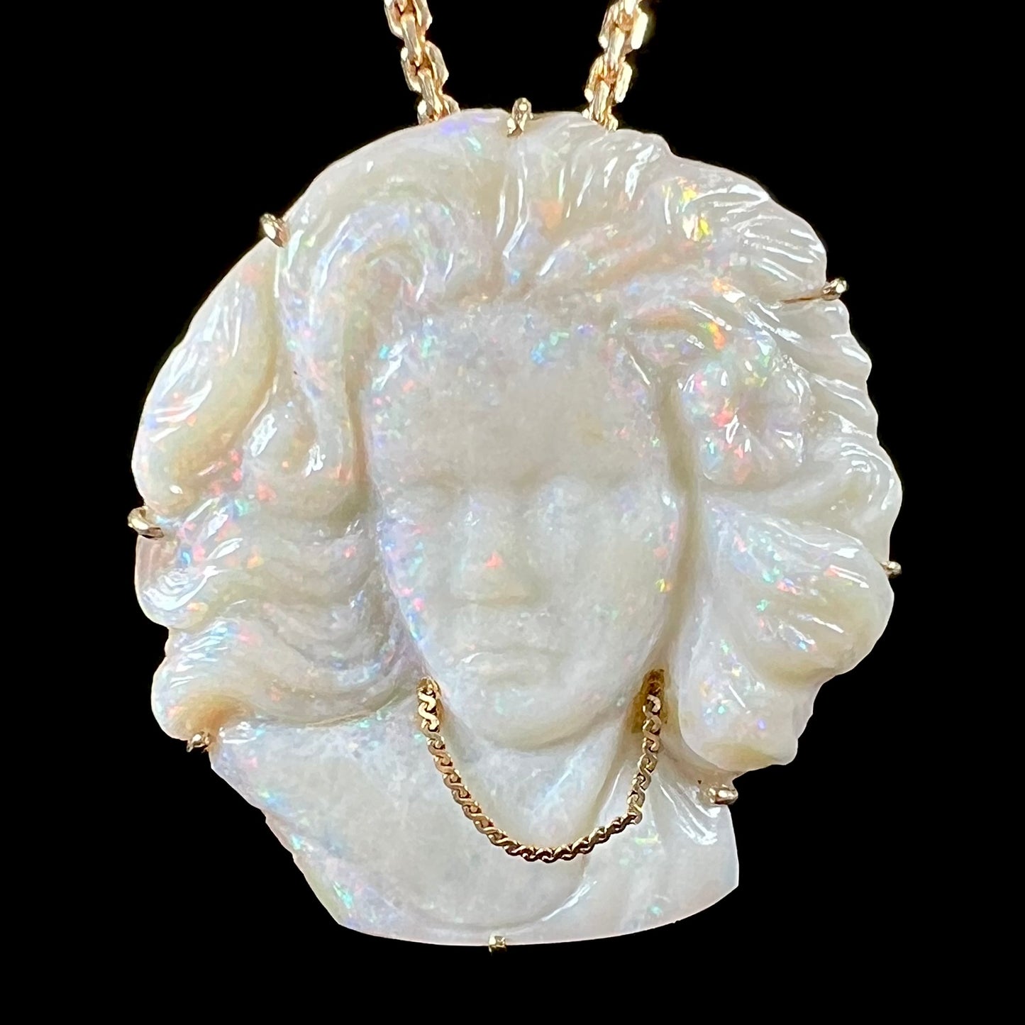 A cameo necklace carved by white crystal opal and held with gold prongs. The cameo is wearing a gold chain.