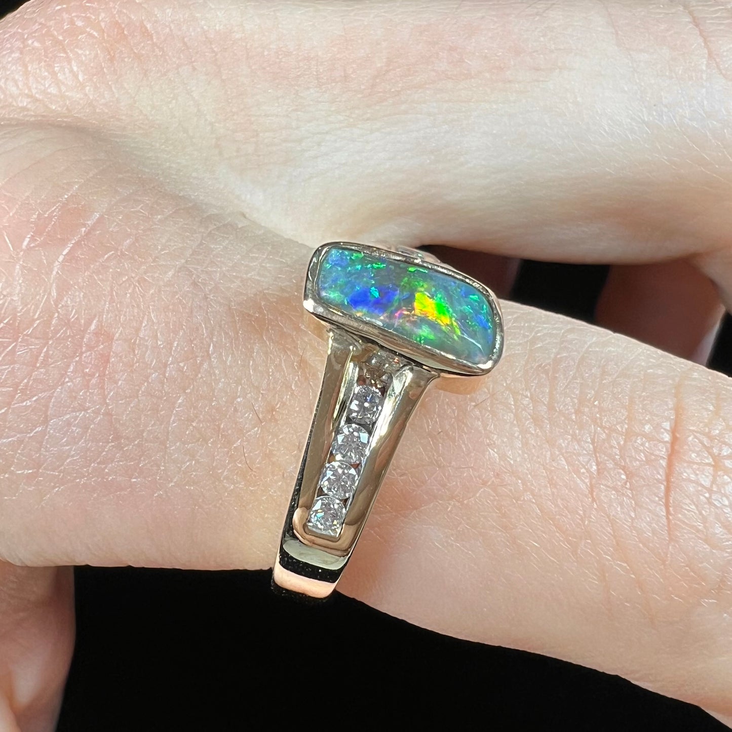 A ladies' yellow gold Australian black crystal opal ring channel set with diamond accent stones.