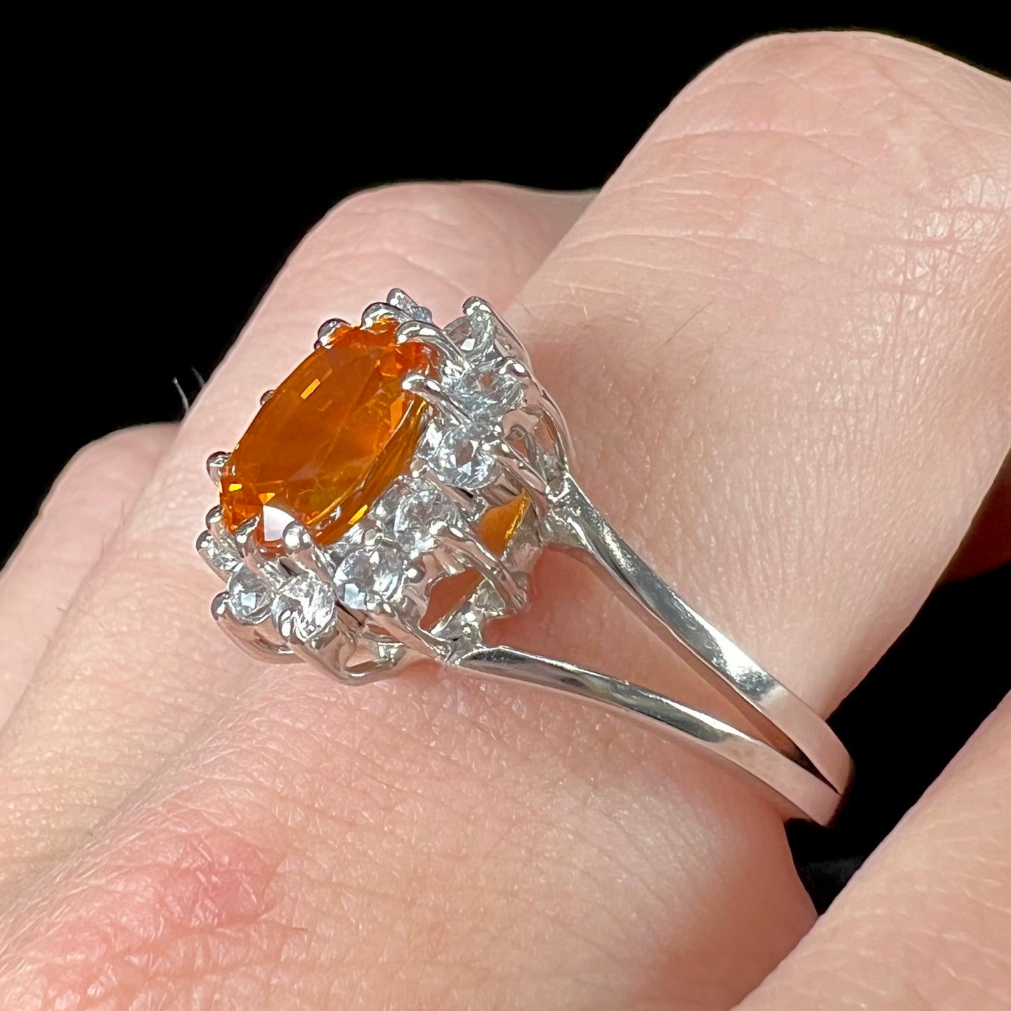 A white gold split shank ring set with an oval cut orange sapphire and a halo of white sapphires.