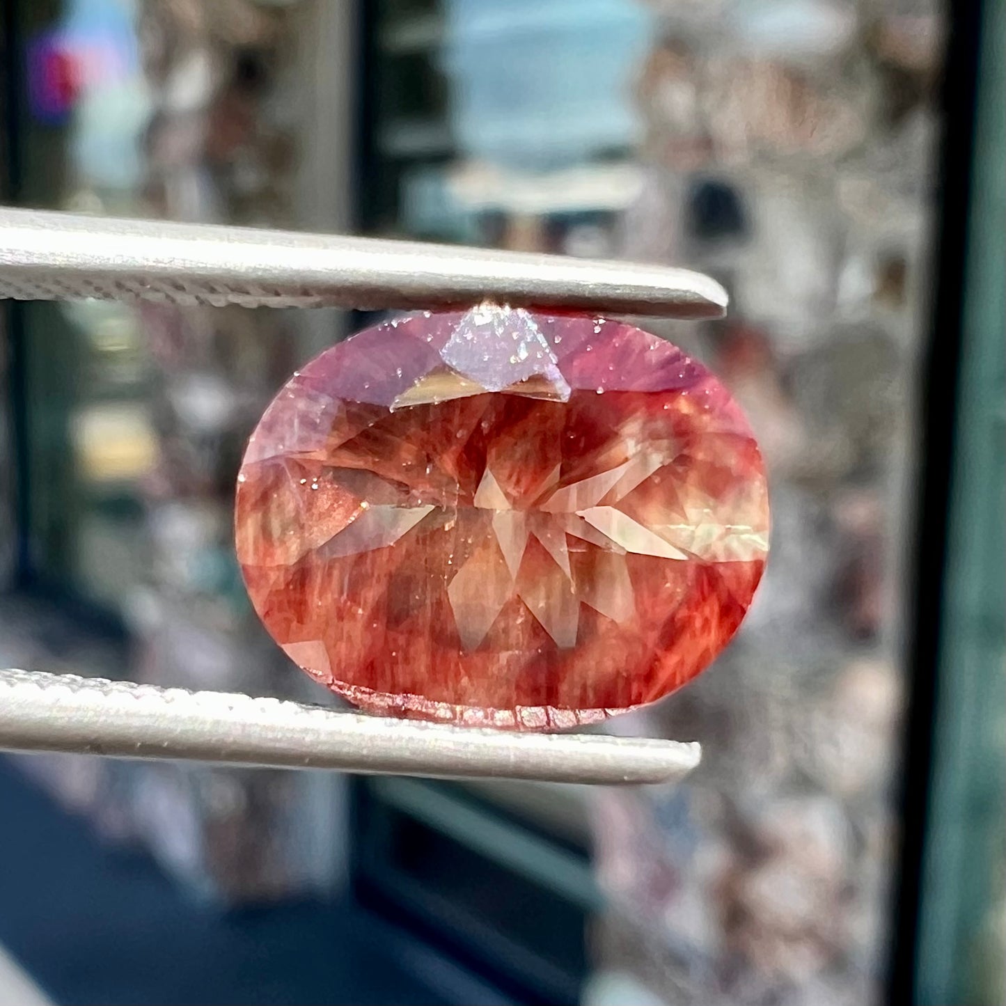 A loose, oval cut oregon sunstone.  The gem is reddish orange with a green secondary color.