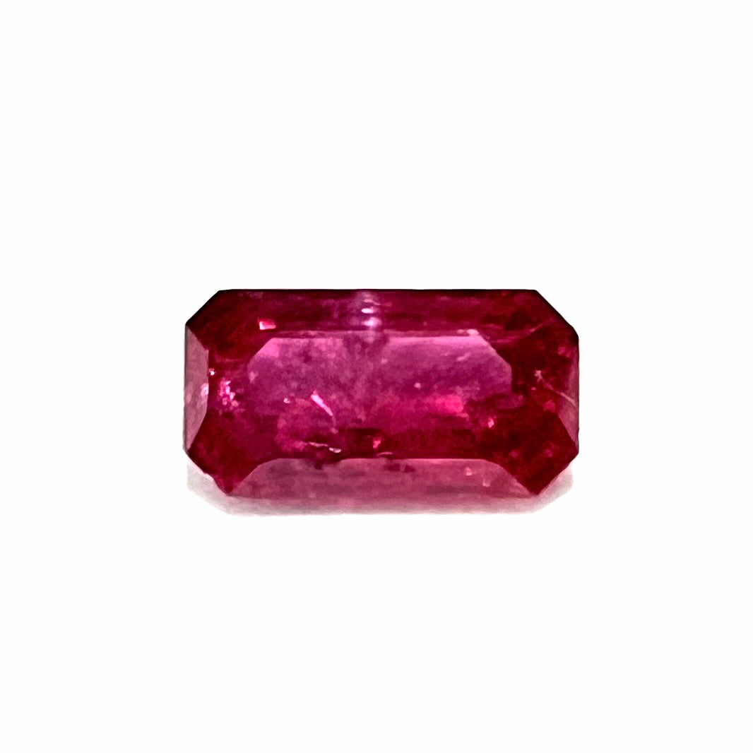 A loose, purplish red natural ruby gemstone. The stone is emerald cut.