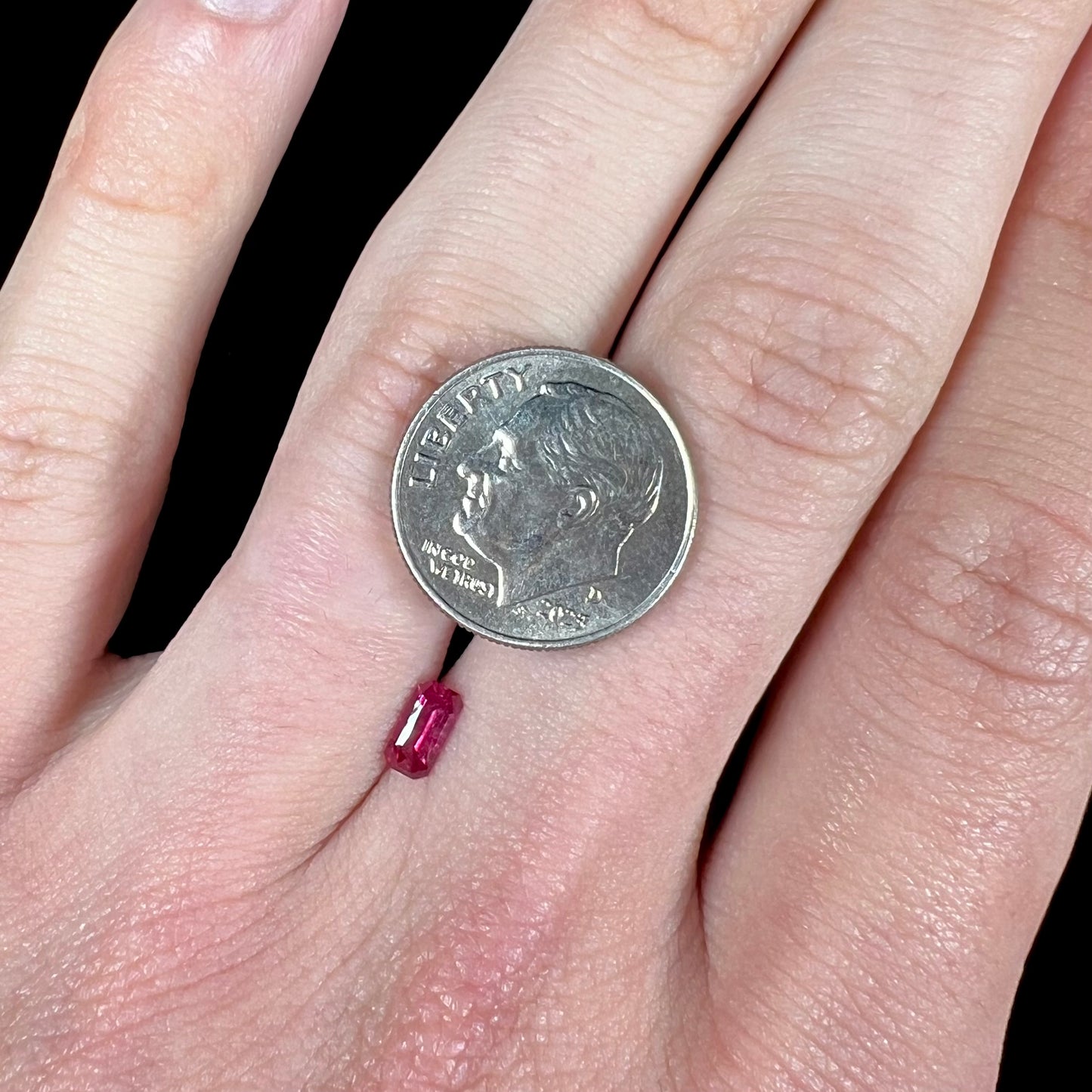 A loose, purplish red natural ruby gemstone. The stone is emerald cut.