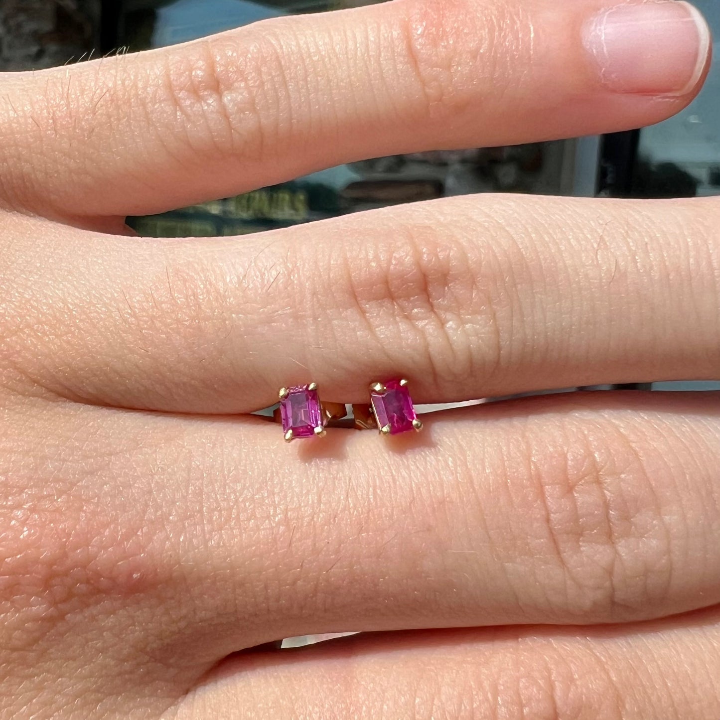 A pair of yellow gold stud earrings set with pinkish red Burmese rubies.  The rubies are emerald cut.