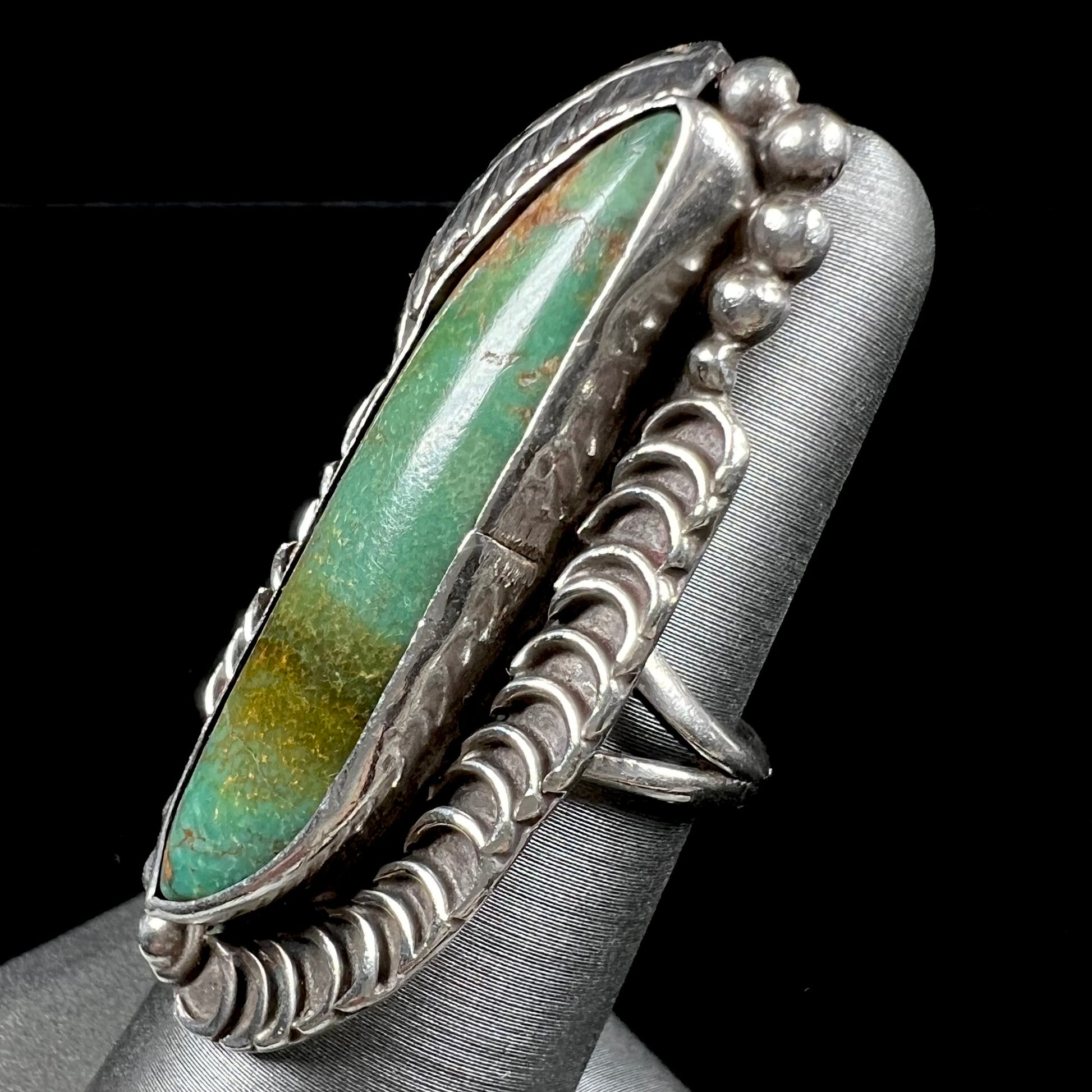 A sterling silver Navajo style ring set with a turquoise stone that shows colors of green, yellow, and reddish brown.