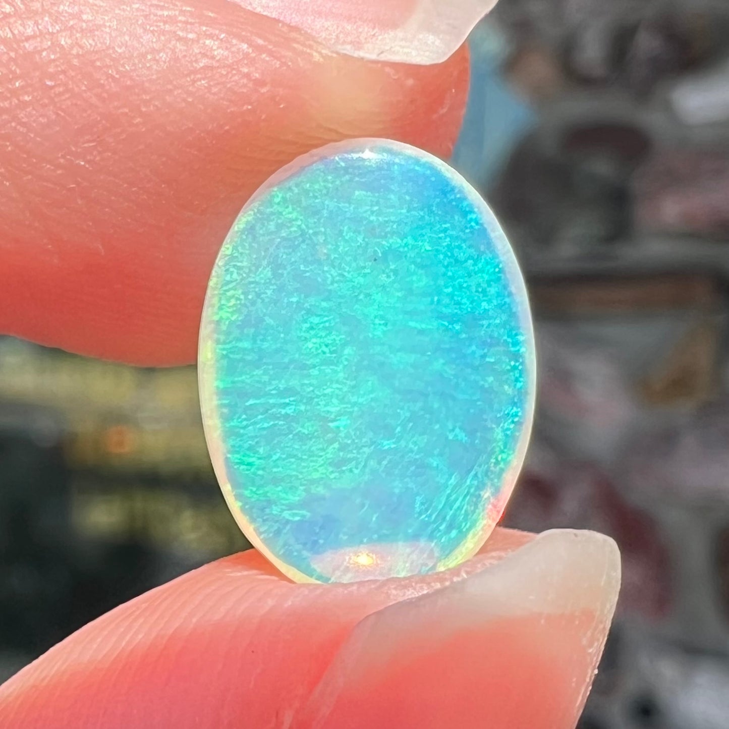 A loose, oval cabochon cut crystal opal from Coober Pedy, Australia. The opal has green and blue colors.