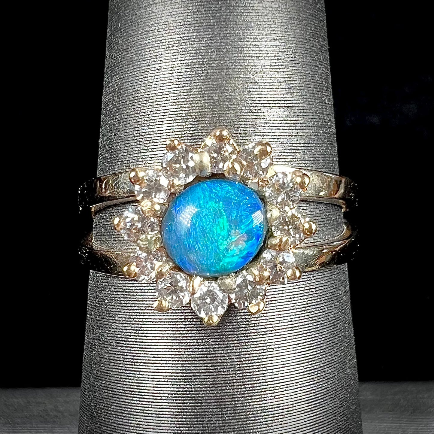 A ladies' round cut black opal and diamond halo ring. The ring is yellow gold and has a split shank.