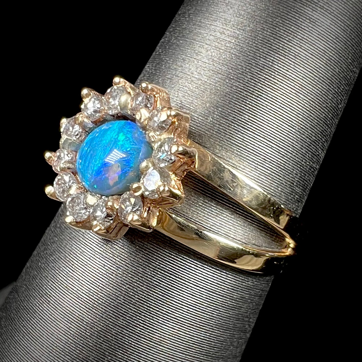 A ladies' round cut black opal and diamond halo ring. The ring is yellow gold and has a split shank.