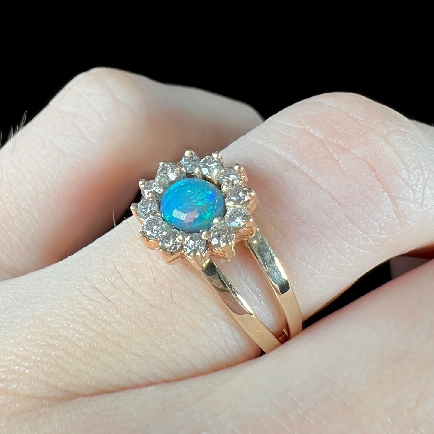 A ladies' round cut black opal and diamond halo ring. The ring is yellow gold and has a split shank.