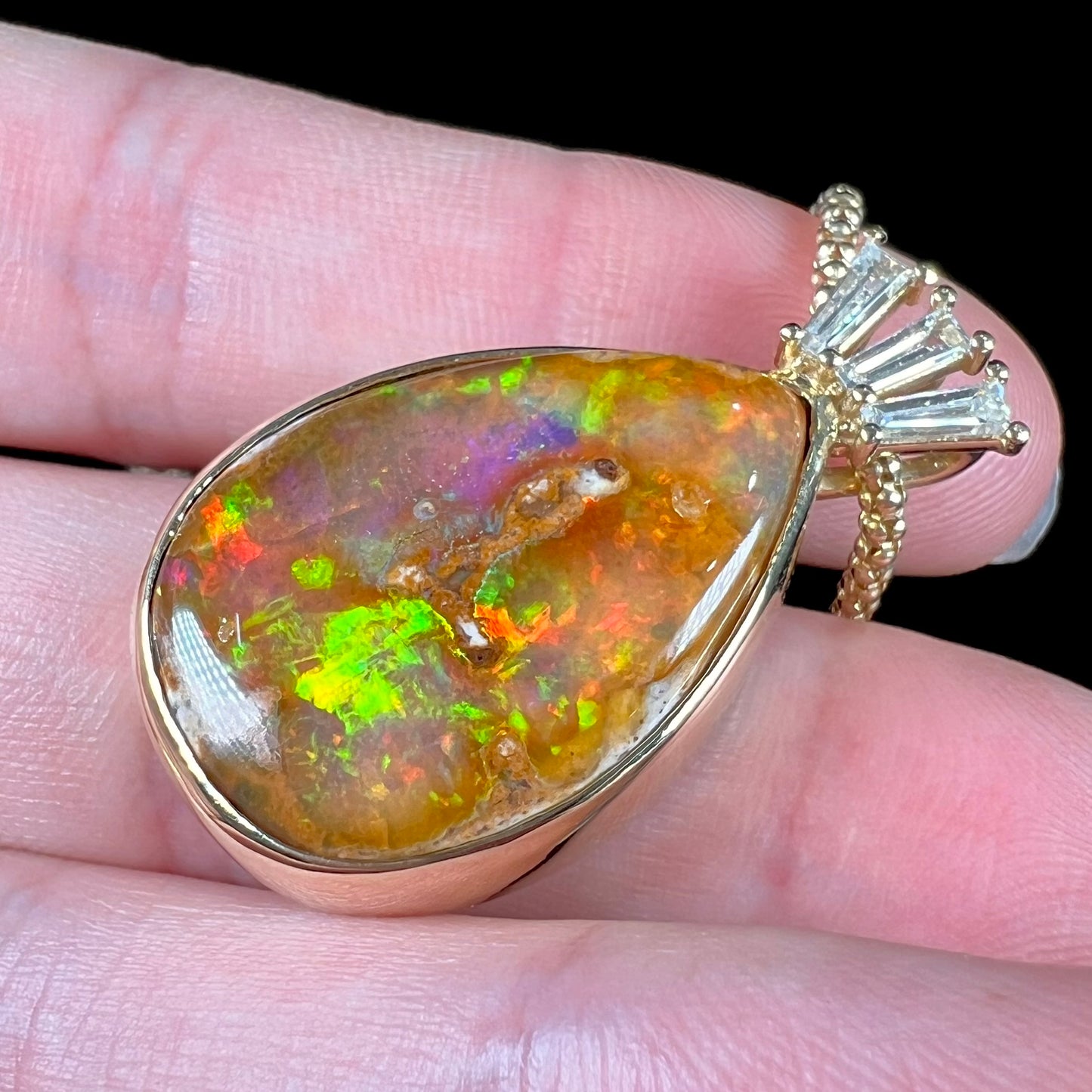 A unisex pear shaped fire opal pendant set with tapered baguette cut diamond accents in 18 karat gold.