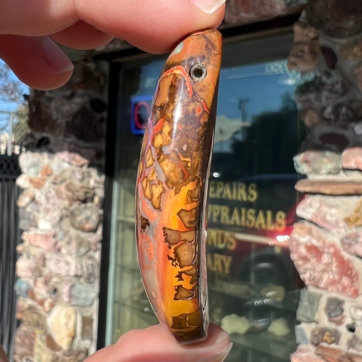 A polished boulder opal stone from Koroit, Australia. The stone has been drilled with a bead hole.