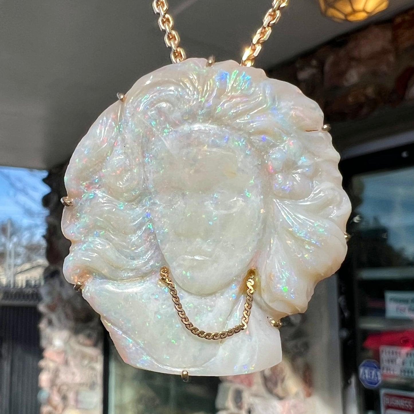 A cameo necklace carved by white crystal opal and held with gold prongs. The cameo is wearing a gold chain.