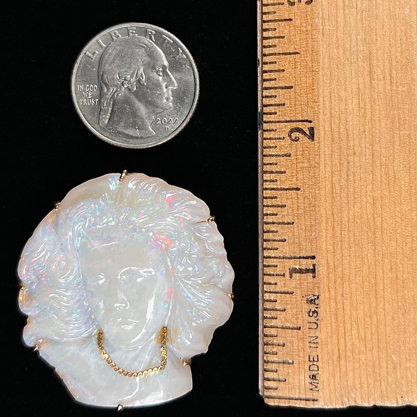 A cameo necklace carved by white crystal opal and held with gold prongs. The cameo is wearing a gold chain.