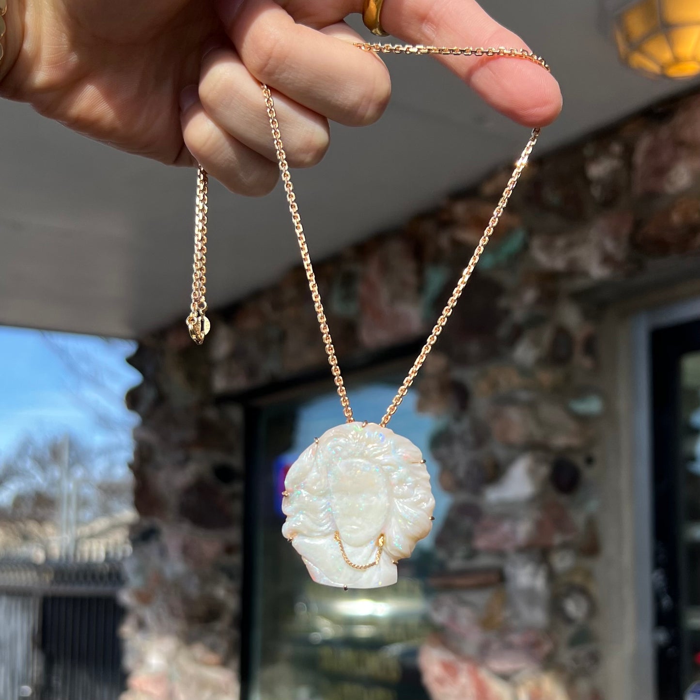 A cameo necklace carved by white crystal opal and held with gold prongs. The cameo is wearing a gold chain.