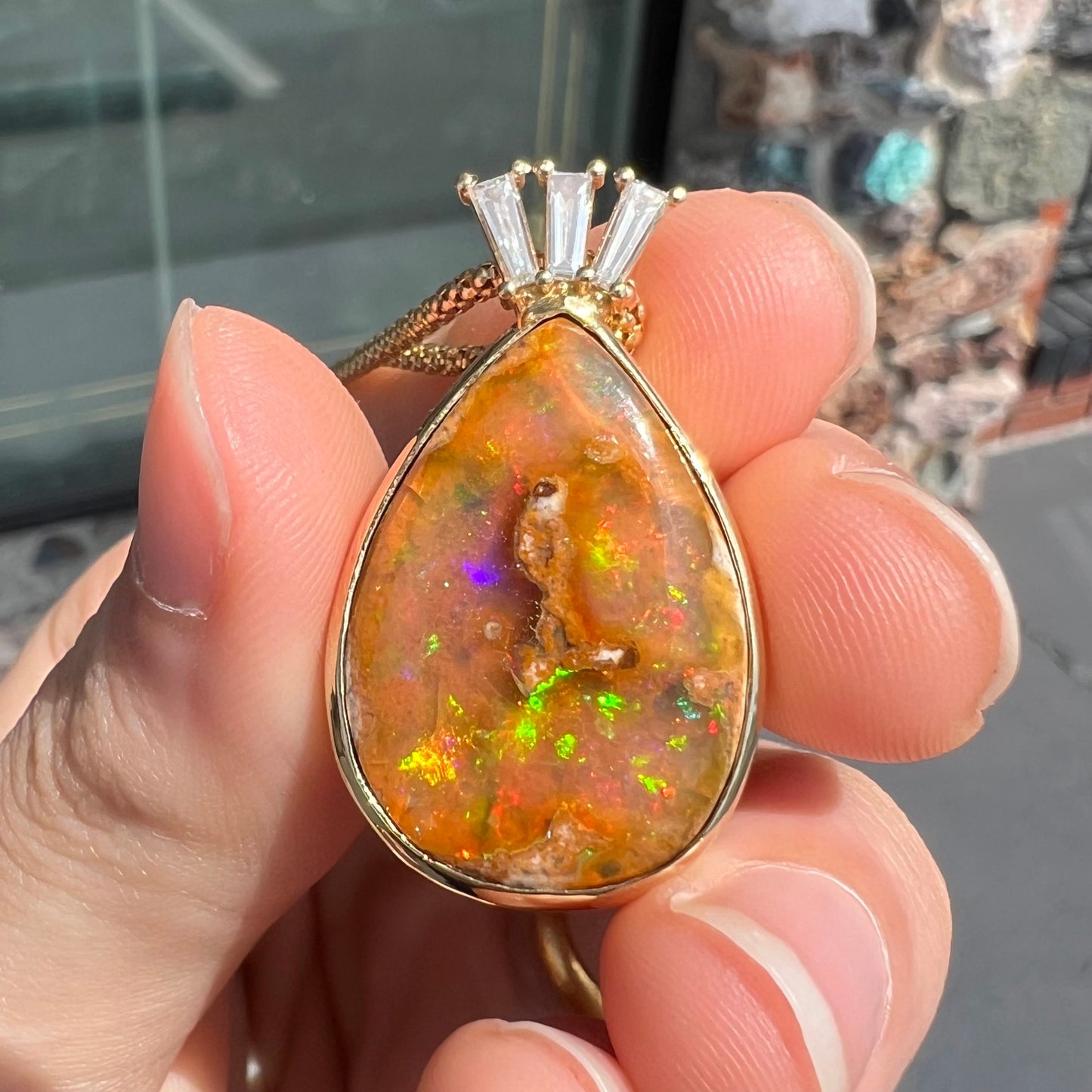 A unisex pear shaped fire opal pendant set with tapered baguette cut diamond accents in 18 karat gold.