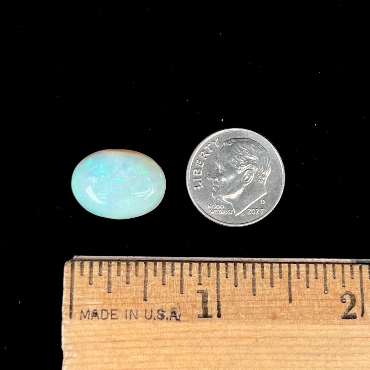An oval cabochon cut white opal stone from Coober Pedy, Australia. The opal has subtle colors of green and blue.