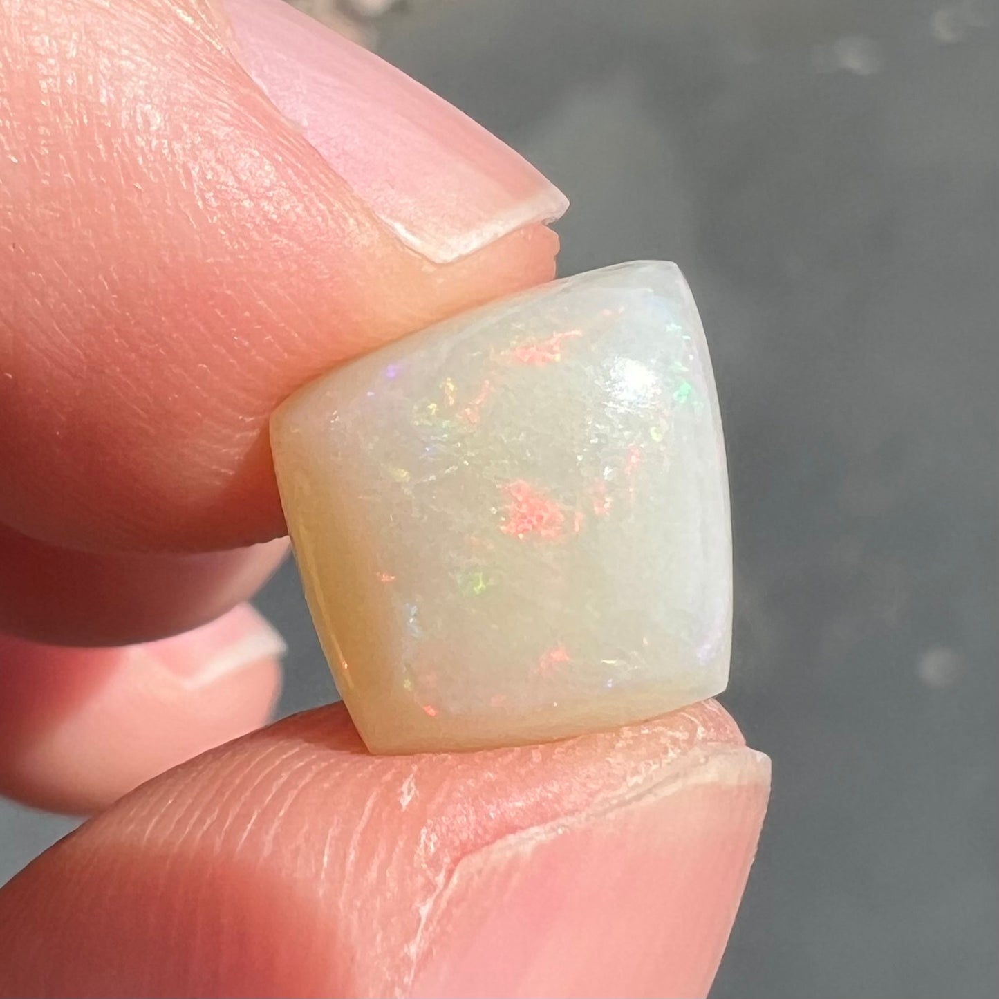A loose, kite shaped white opal stone from Coober Pedy, Australia. The stone has subdued red colors.