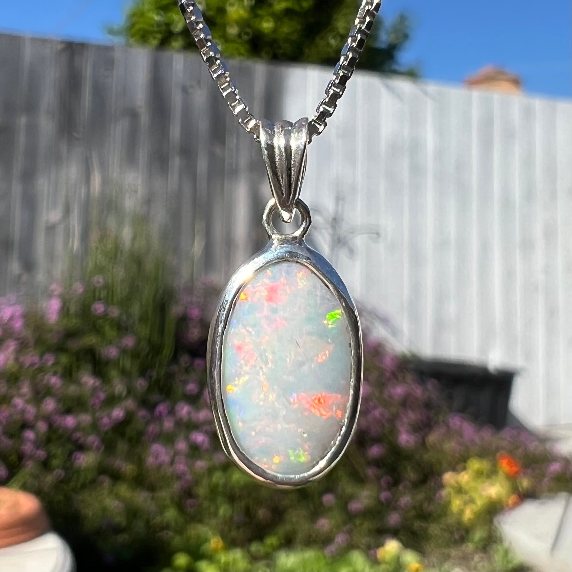 A ladies' sterling silver necklace bezel set with a natural white crystal opal.  The opal has red and blue fire.