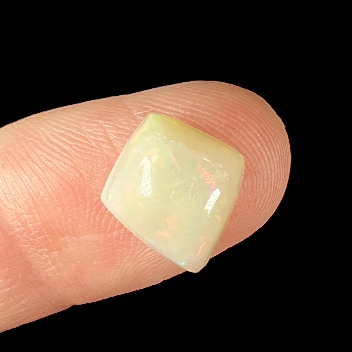 A loose, kite shaped white opal stone from Coober Pedy, Australia. The stone has subdued red colors.