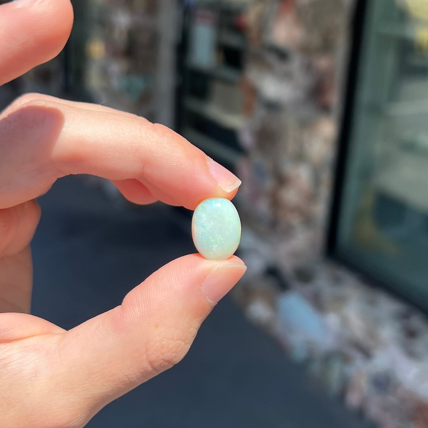 An oval cabochon cut white opal stone from Coober Pedy, Australia. The opal has subtle colors of green and blue.