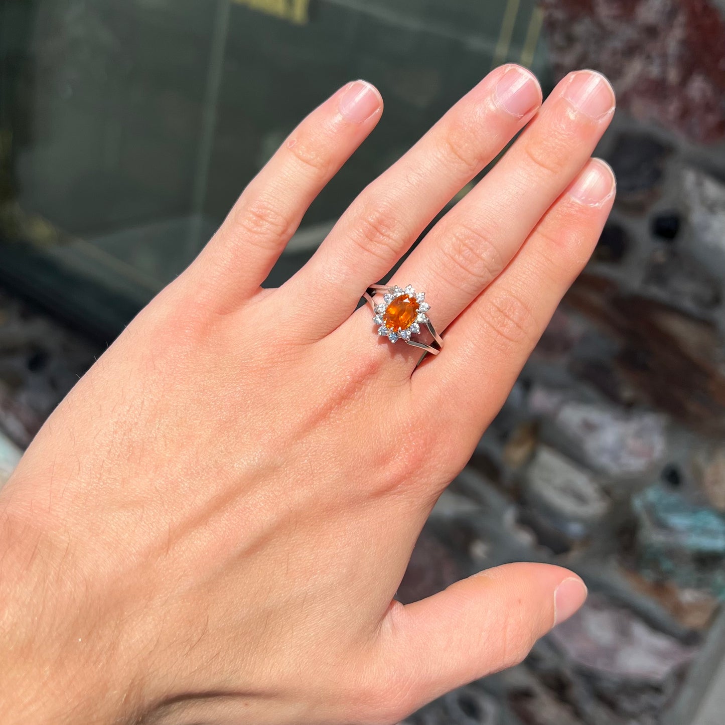 A white gold split shank ring set with an oval cut orange sapphire and a halo of white sapphires.