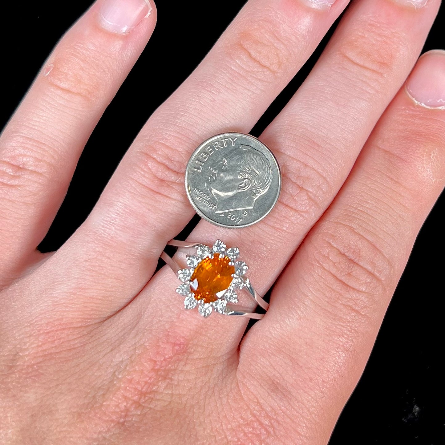 A white gold split shank ring set with an oval cut orange sapphire and a halo of white sapphires.