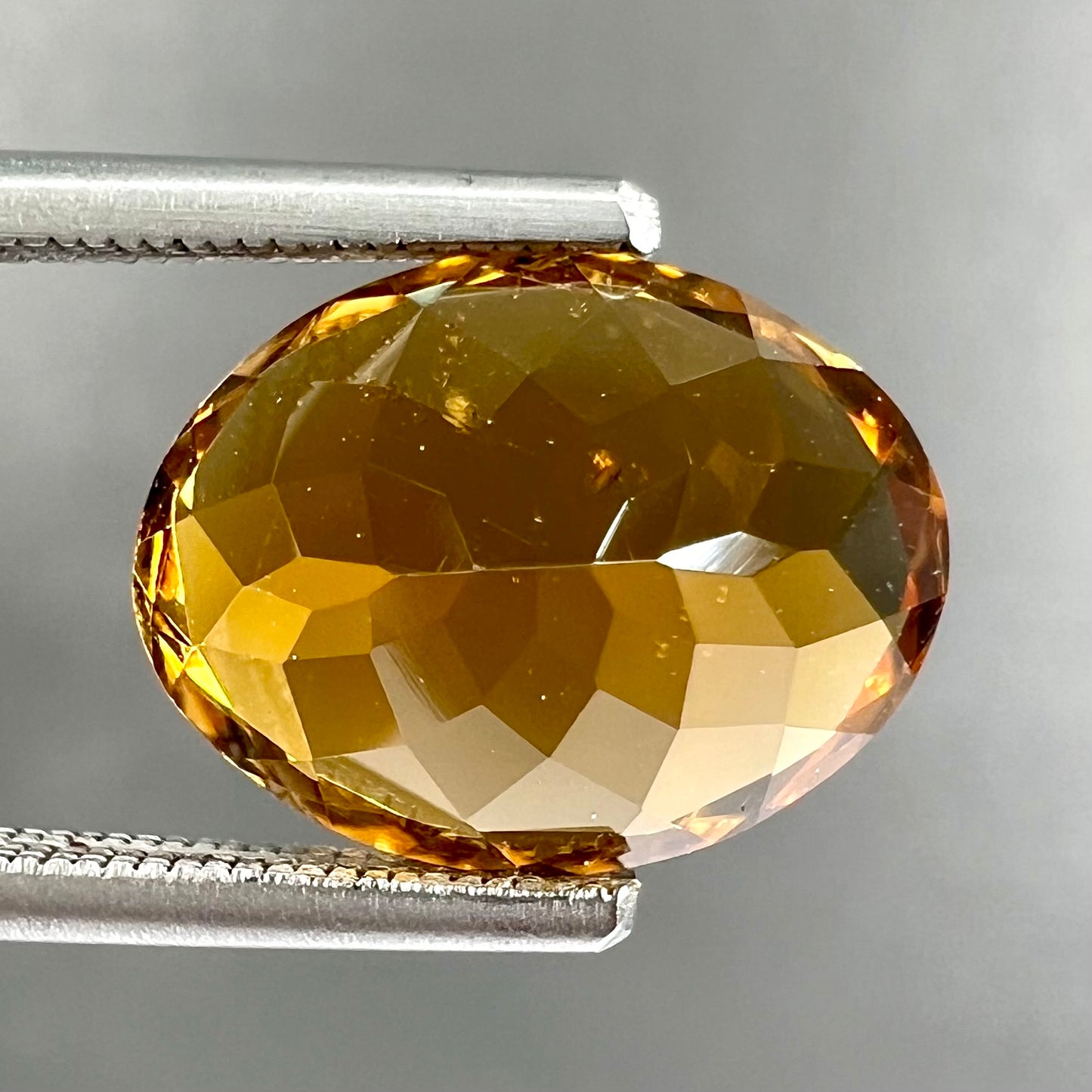 A loose, faceted oval cut orange dravite tourmaline gemstone.