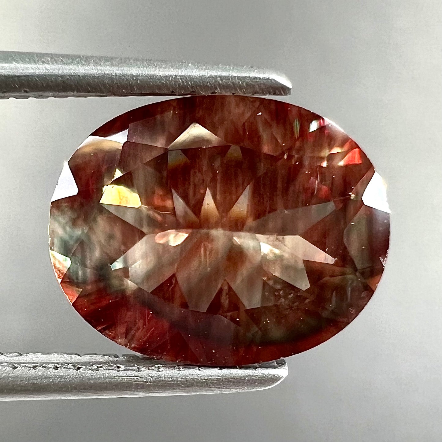 A loose, oval cut oregon sunstone.  The gem is reddish orange with a green secondary color.