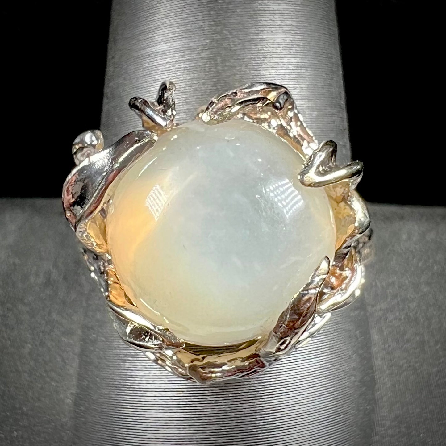A ladies' organic style white gold moonstone ring. The moonstone shows white adularescence on a creamy white body color. Prongs resemble leaves holding the stone.