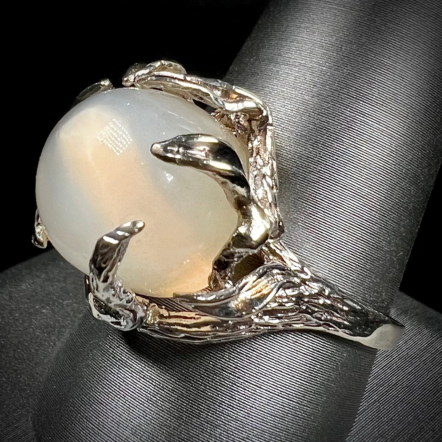 A ladies' organic style white gold moonstone ring. The moonstone shows white adularescence on a creamy white body color. Prongs resemble leaves holding the stone.