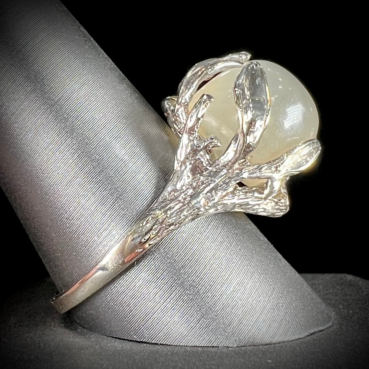 A ladies' organic style white gold moonstone ring. The moonstone shows white adularescence on a creamy white body color. Prongs resemble leaves holding the stone.