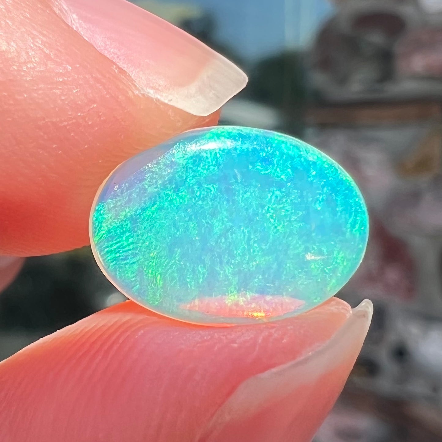 A loose, oval cabochon cut crystal opal from Coober Pedy, Australia. The opal has green and blue colors.