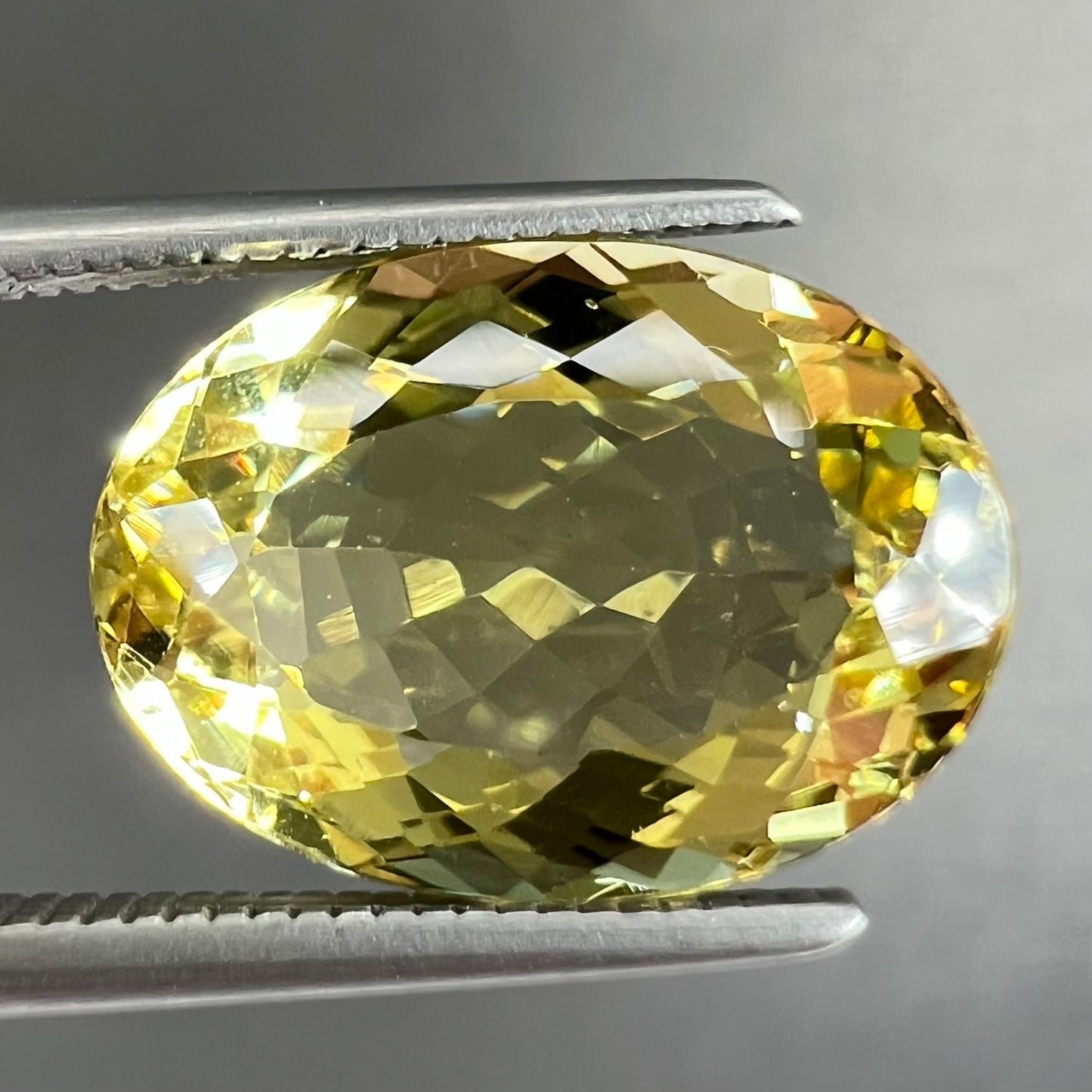 A faceted oval cut golden beryl gemstone. The stone is a greenish light yellow.