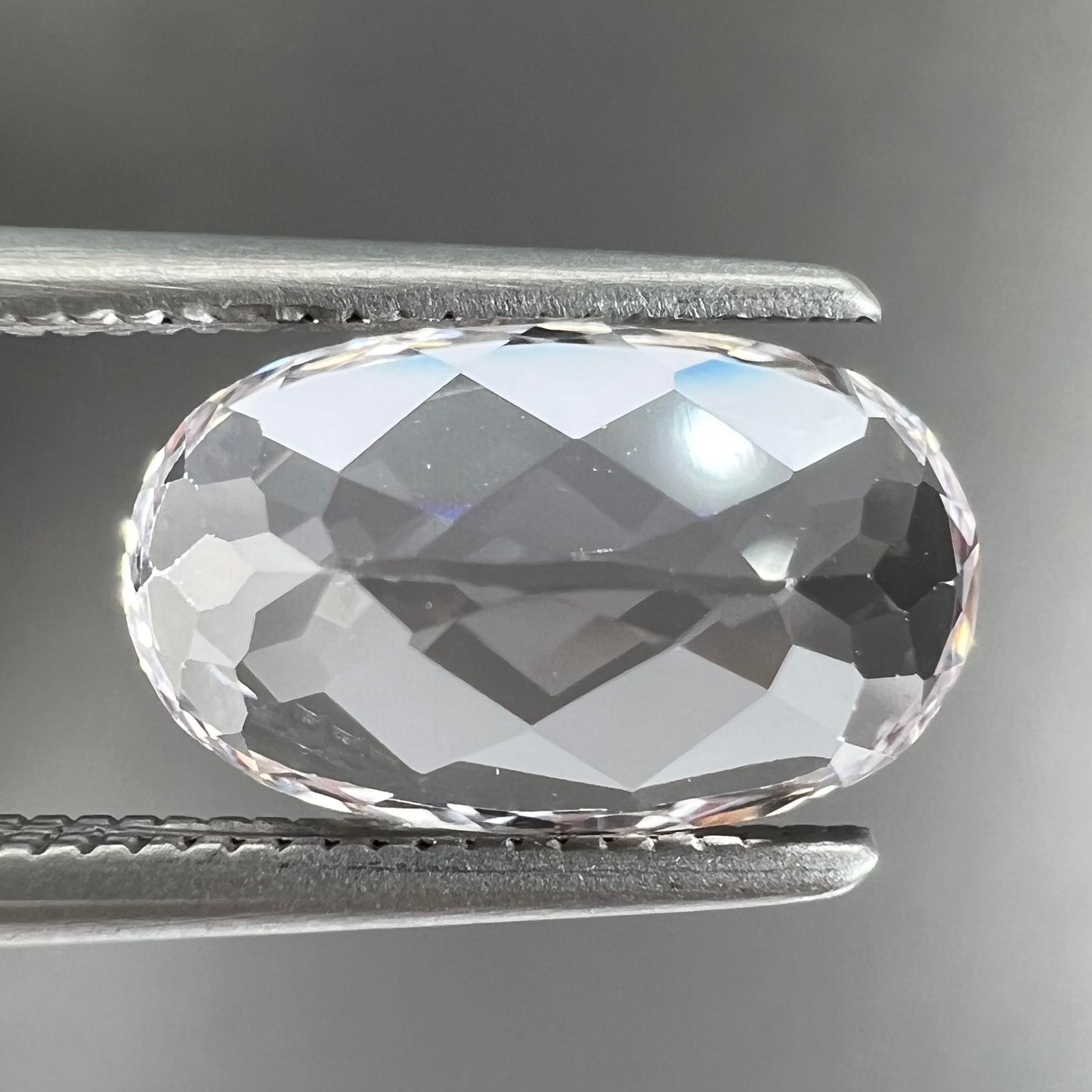 A loose, faceted oval cut kunzite gemstone. The stone is a light pink color.