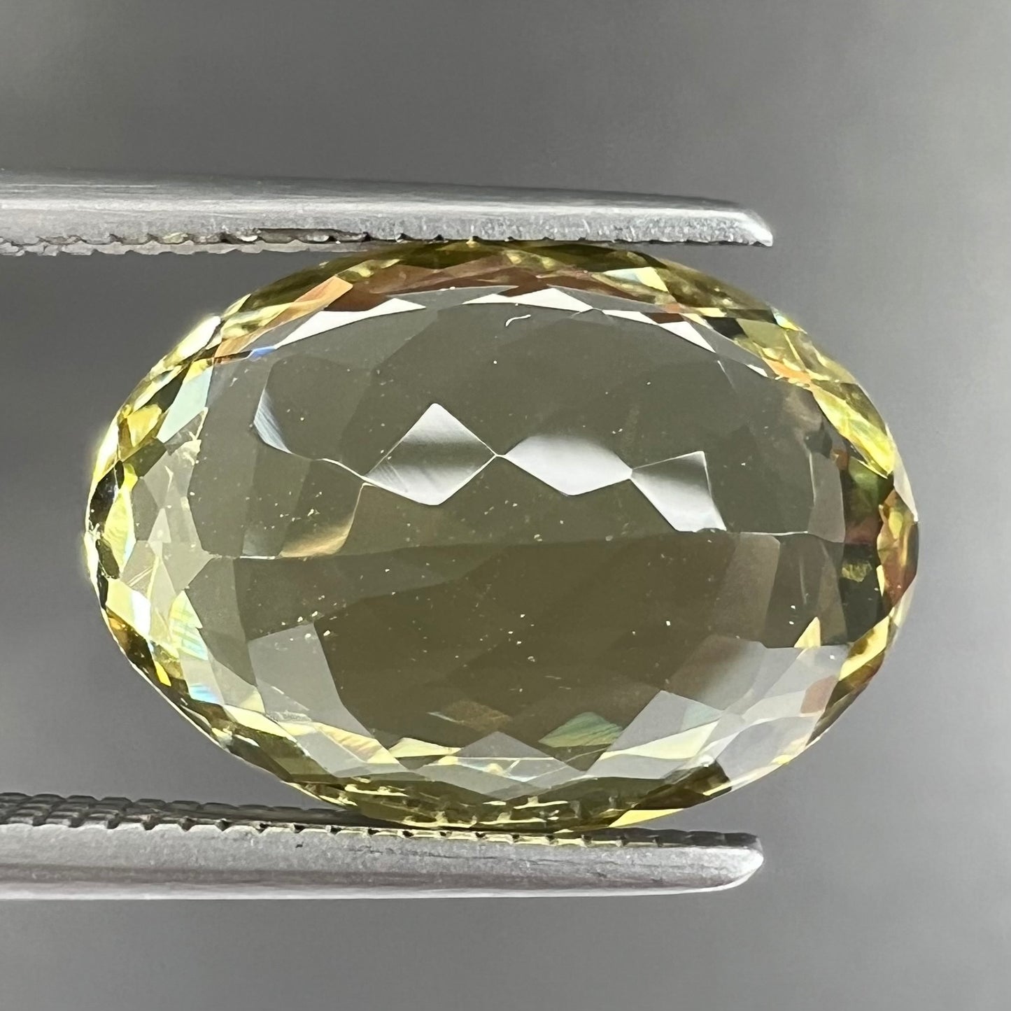A faceted oval cut golden beryl gemstone. The stone is a greenish light yellow.