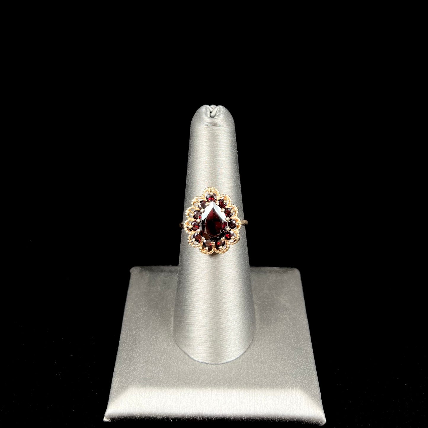 A vintage, 1940's style yellow gold ring set with a pear shaped almandine garnet. A halo of round garnets surround the center stone.