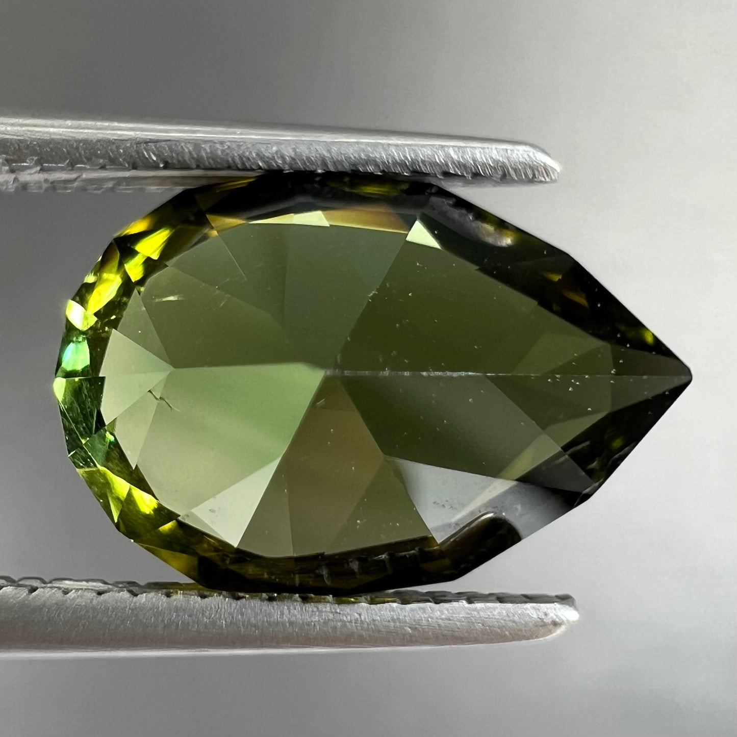 A loose, pear shaped green tourmaline gemstone. The color is dark green with a yellow secondary hue.