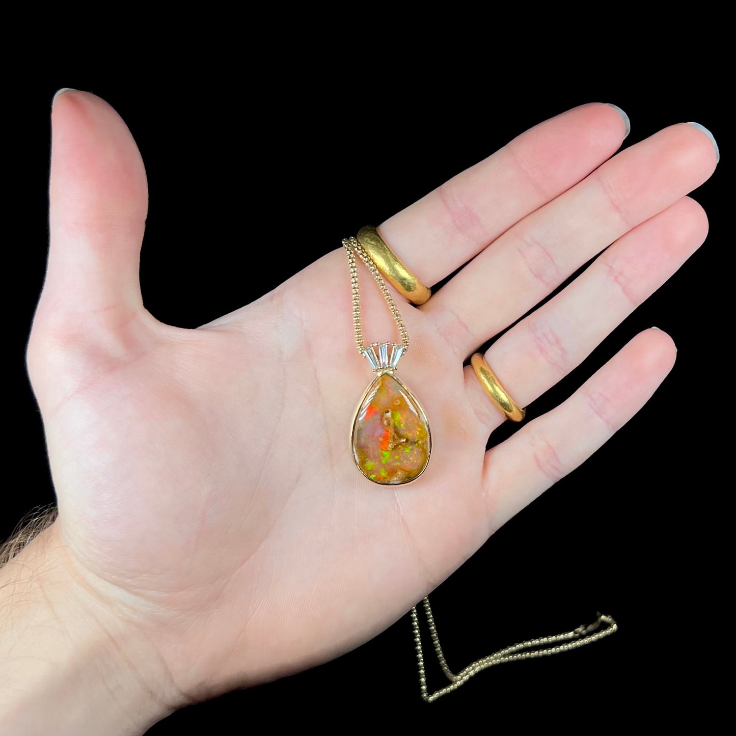 A unisex pear shaped fire opal pendant set with tapered baguette cut diamond accents in 18 karat gold.
