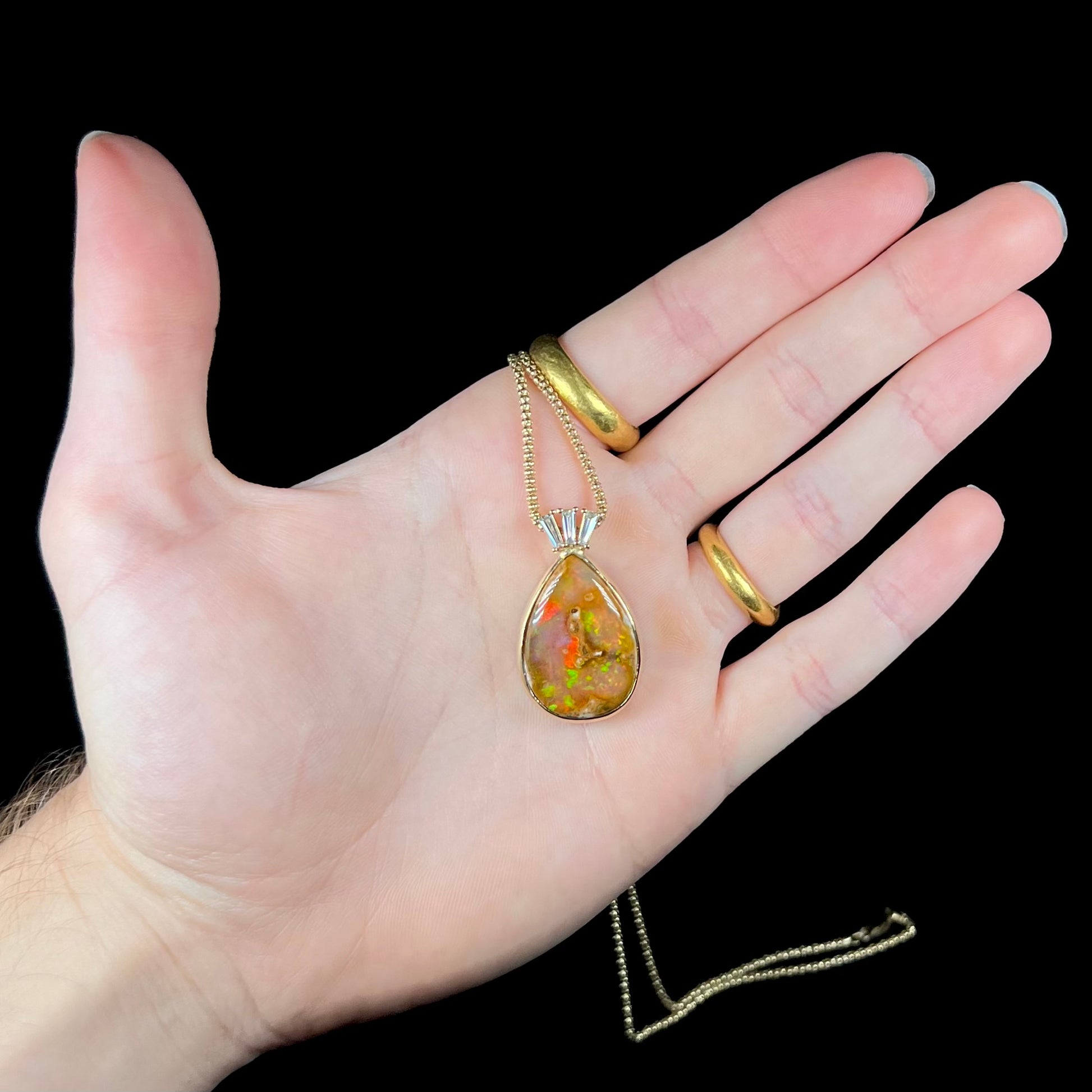 A unisex pear shaped fire opal pendant set with tapered baguette cut diamond accents in 18 karat gold.